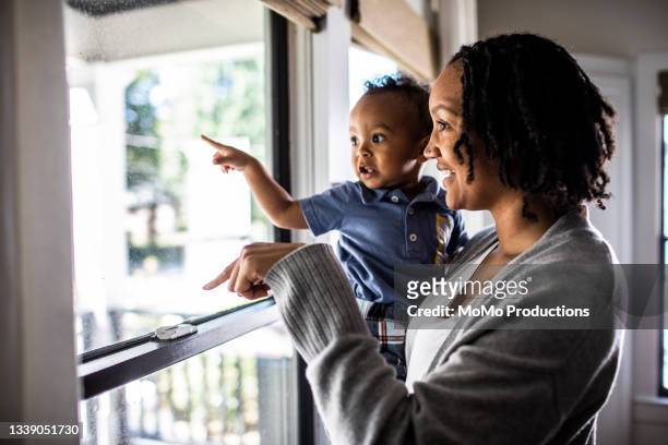 mother and toddler looking out of home window - blick durchs fenster aussenaufnahme haus stock-fotos und bilder