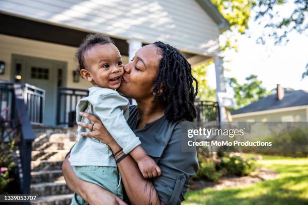 mother holding toddler in front of new home - familie baby stock-fotos und bilder