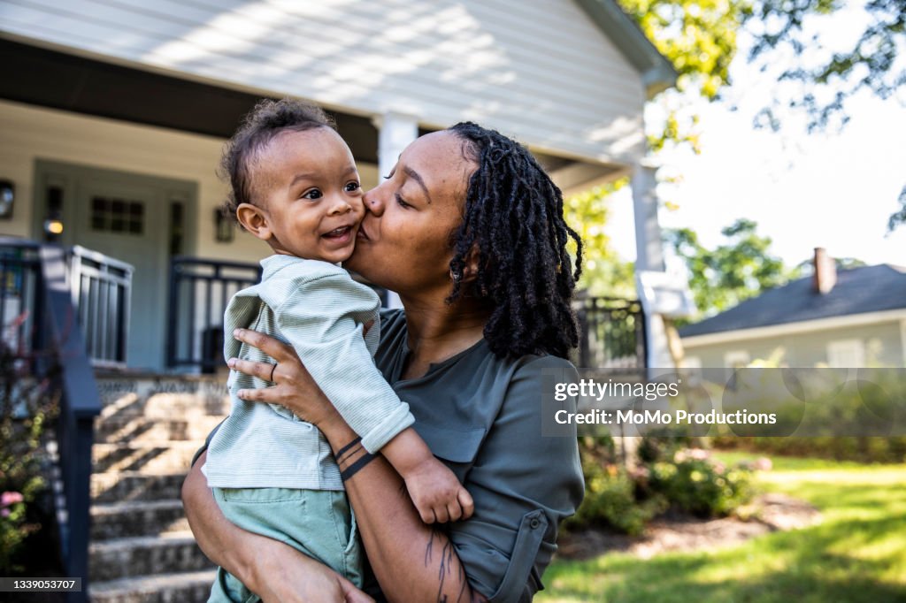 Mother holding toddler in front of new home
