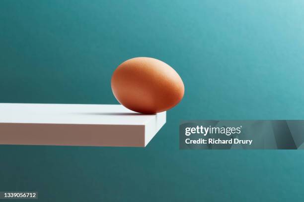 an egg teetering on the edge of a plank - risk concept stock pictures, royalty-free photos & images