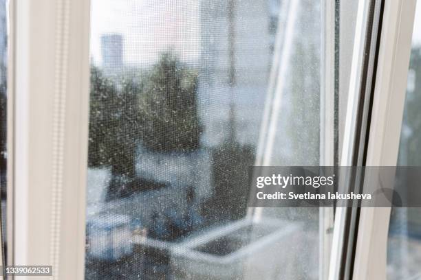 photo of a glass of a dirty plastic white window in the morning. glass and mosquito netting in dust, dirt and streaks. against the background of dirt, a street with houses and trees. - mosquito netting stock-fotos und bilder