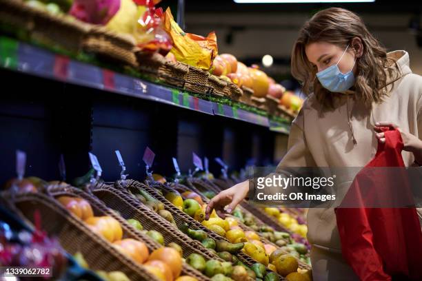 woman wearing protective face mask shopping for fruit in the supermarket - atemmaske stock-fotos und bilder