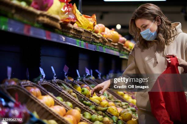 woman wearing protective face mask shopping for fruit in the supermarket - sports clothing retail stock pictures, royalty-free photos & images