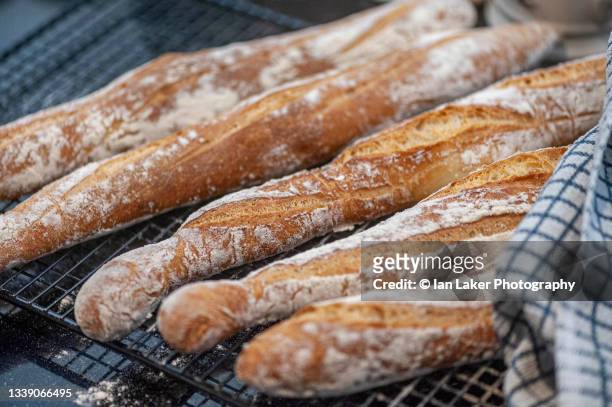littlebourne, kent, england, uk. 19 june 2021. fresh baguettes cooling on a wire rack. - barra de pan francés fotografías e imágenes de stock