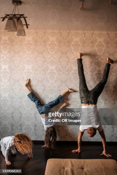 father with two girls doing a handstand at home - équilibre sur les mains photos et images de collection