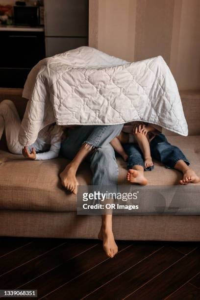 unrecognizable mother with girls under blanket on sofa at home - viso nascosto foto e immagini stock