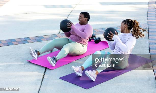 two african-american woman exercising with medicine ball - sit ups stockfoto's en -beelden