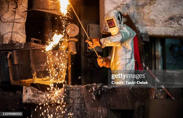 mature adult male metallurgist in protective workwear checking molten metal in foundry - foundry worker stock pictures, royalty-free photos & images