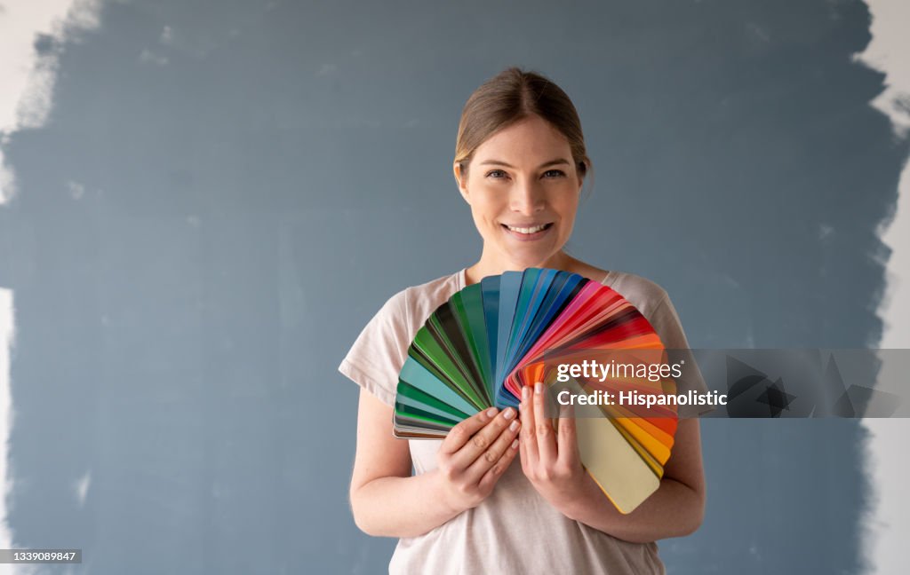 Glückliche Frau, die ihr Haus malt und eine Farbe aus einer Palette wählt