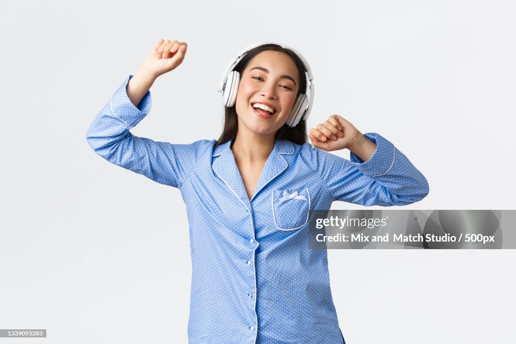 Young woman listening music while standing against white background