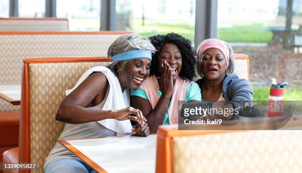 senior african-american women in diner looking at smart phone - african american restaurant texting stockfoto's en -beelden