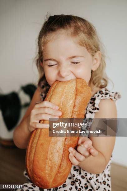 portrait of a little girl who bites a whole loaf of bread. the child is eating bread. close-up photo. - young tiny girls photos et images de collection