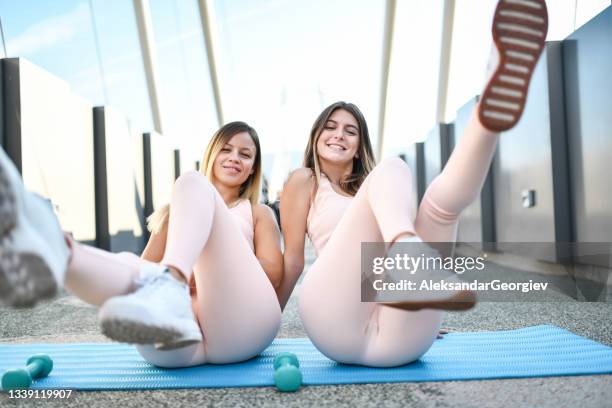 smiling female athletes stretching legs during outdoor bridge workout - female soles stockfoto's en -beelden