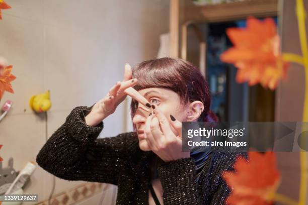 close-up of young woman in her bedroom inserting contact lens for halloween costume - contacts stock-fotos und bilder