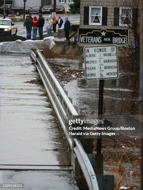 Lowell residents watch as the risen waters of the Beaver Brook are contained by dikes as they flow into the Merrimac at Beaver St.