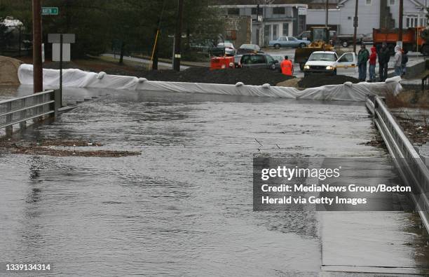 Lowell residents watch as the risen waters of the Beaver Brook are contained by dikes as they flow into the Merrimac at Beaver St. A bucket loader...