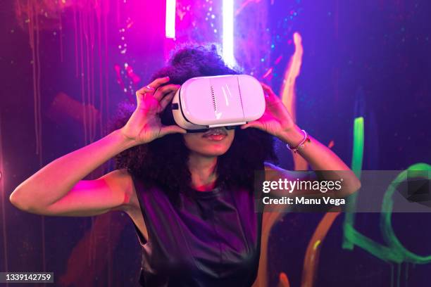 shocked female wearing vr goggles touching air while experiencing cyberspace in studio with neon illumination - virtual fotografías e imágenes de stock