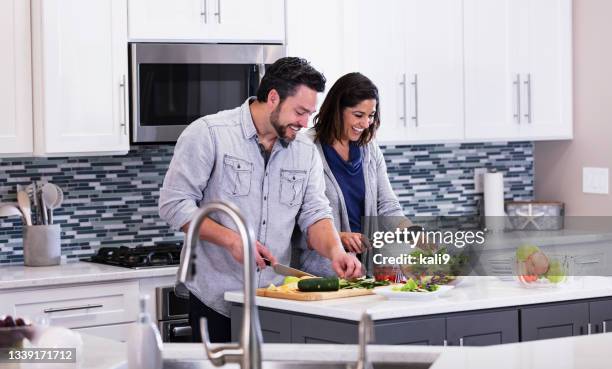 multiracial couple in kitchen making salad, conversing - healthy older couple stock pictures, royalty-free photos & images