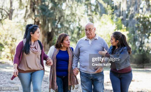 senior hispanic couple walk with adult daughters at park - family serious stock pictures, royalty-free photos & images