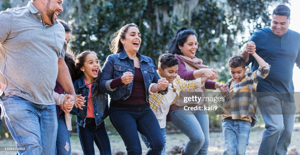 Large Hispanic family running, laughing at the park