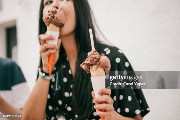 pretty latina stands on street holding melting chocolate cone ice cream - ice cream cone stockfoto's en -beelden