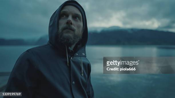bearded fisherman portrait: with raincoat by a fjord at night - visser stockfoto's en -beelden