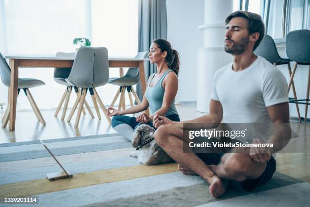 young couple meditating in lotus position at home. - sport tablet stockfoto's en -beelden