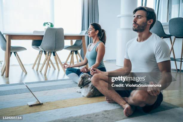 young couple meditating in lotus position at home. - couple doing yoga stock pictures, royalty-free photos & images