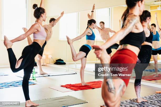 group of people balancing on one leg during yoga class - yoga caliente fotografías e imágenes de stock