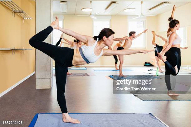 woman standing on one leg balancing during hot yoga class - yoga caliente fotografías e imágenes de stock