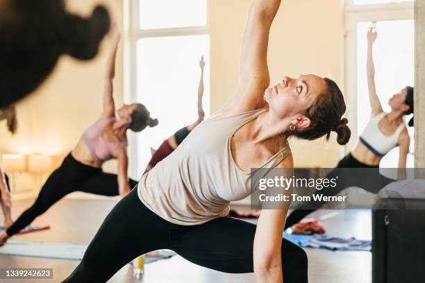 woman posing with one arm raised in yoga class - yoga studio stock-fotos und bilder