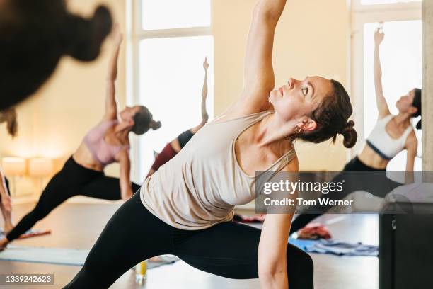 woman posing with one arm raised in yoga class - yoga caliente fotografías e imágenes de stock