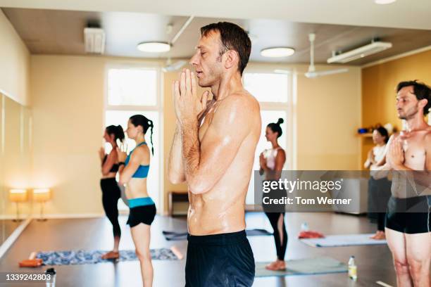 man posing in praying position during hot yoga class - bikram yoga stock pictures, royalty-free photos & images