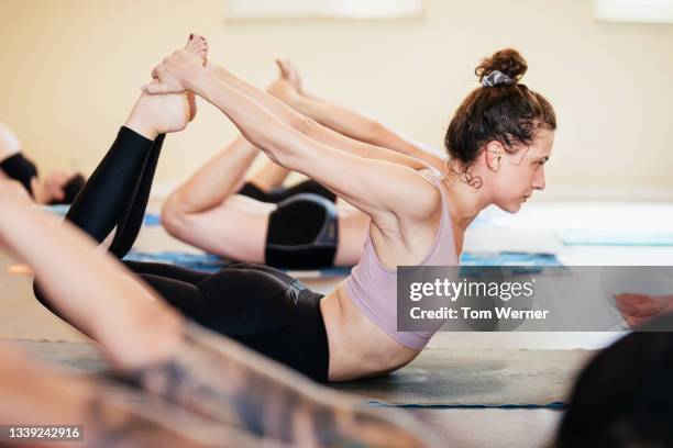 woman on stomach grasping feet from behind during yoga class - woman lying on stomach with feet up foto e immagini stock