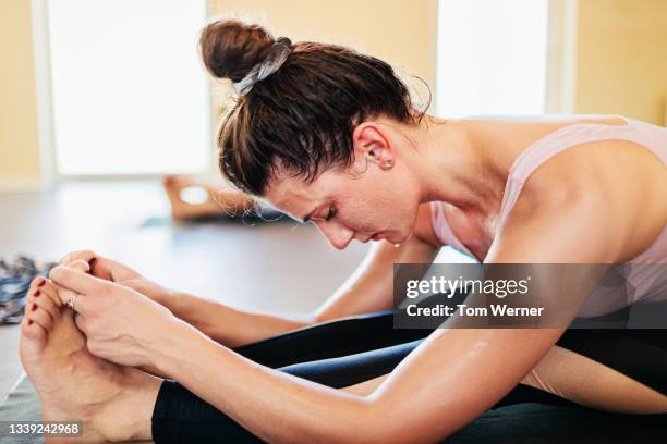 woman touching toes during hot yoga class - hot yoga fotografías e imágenes de stock