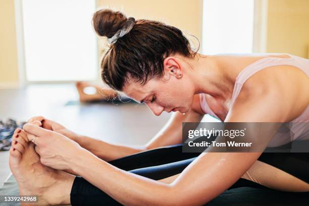 woman touching toes during hot yoga class - yoga caliente fotografías e imágenes de stock