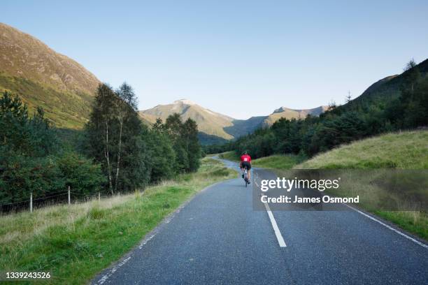 cyclist heading for the mountains on the winding road of glen nevis. - cycling scotland stock pictures, royalty-free photos & images