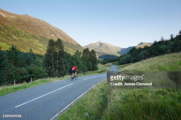 cyclist heading for the mountains on the winding road of glen nevis. - cycling scotland stock pictures, royalty-free photos & images