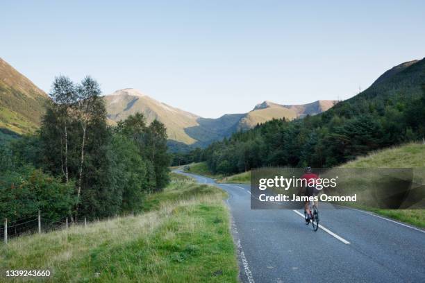 cyclist heading for the mountains on the winding road of glen nevis. - cycling scotland stock pictures, royalty-free photos & images