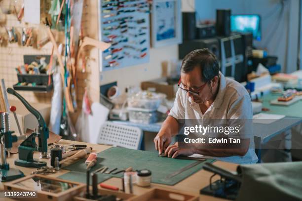 asiatischer chinesischer senior, der in seinem atelier an handgefertigten lederuhrenstreifen arbeitet - ahlen stock-fotos und bilder