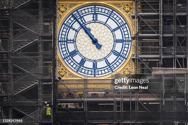 Two people walk down the steps past the restored clock face on Elizabeth Tower, displaying the original Prussian blue colour of the hands, on...