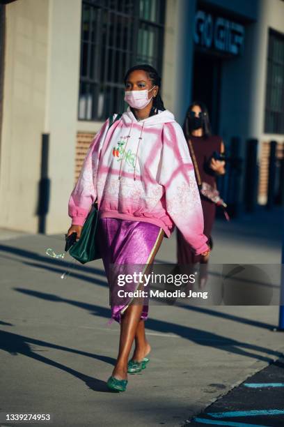 Model Gabrielle Richardson wears a white and pink hoodie with drawings, pink/purple velvet skirt, and green retro jelly slippers outside the Collina...