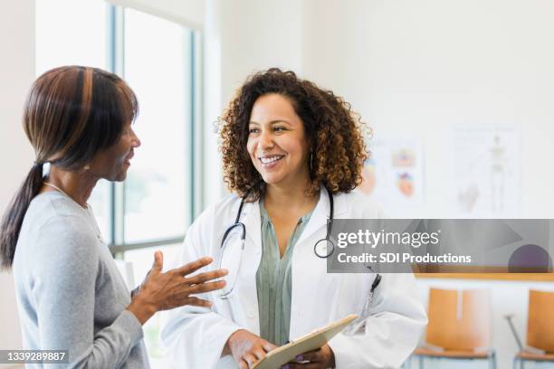 standing together, female doctor smiles while mature female patient speaks - doctor patient bildbanksfoton och bilder