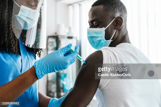 close up view of an adult young man receiving a vaccine at a medical clinic - arm needle stockfoto's en -beelden