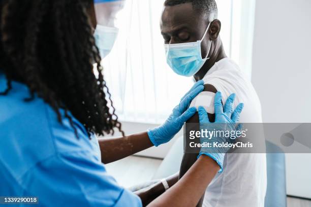 female doctor or nurse putting a bandage after covid-19 vaccination at vaccination center - black glove stock pictures, royalty-free photos & images