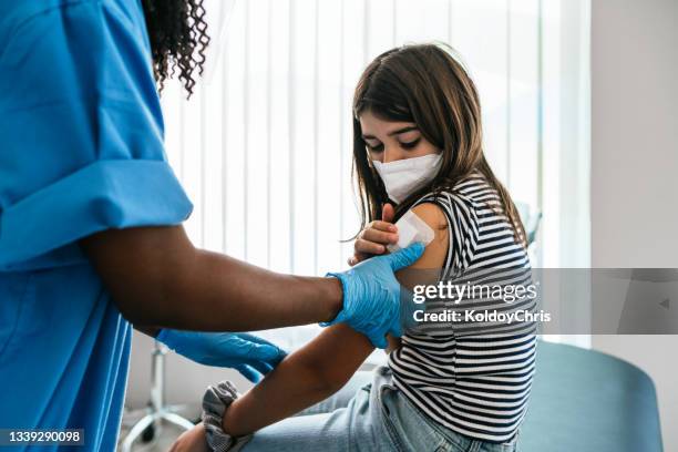 female doctor or nurse putting a bandage after covid-19 vaccination at vaccination center - child vaccine stock pictures, royalty-free photos & images