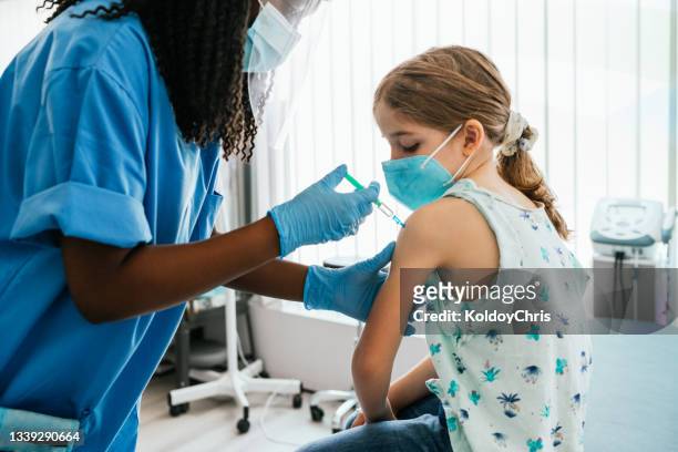 young girl watching her being injected with covid-19 vaccine at a medical clinic - vacuna fotografías e imágenes de stock