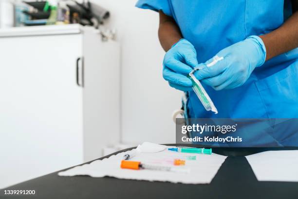 unrecognizable nurse opening disposable syringe wrapper and other disposable materials on gauze for use in vaccinating patients at the vaccination center - material sanitario fotografías e imágenes de stock