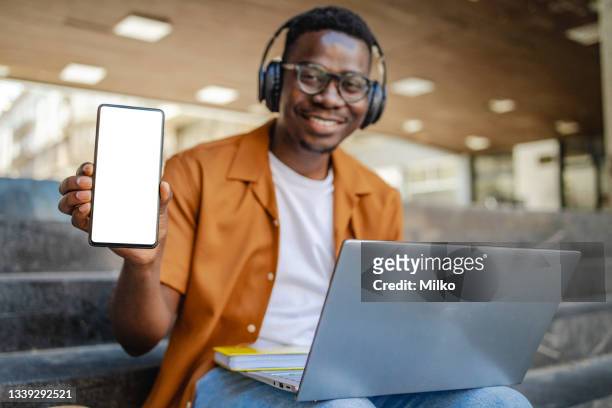 young man holding mobile device with white screen - using laptop and phone stock pictures, royalty-free photos & images
