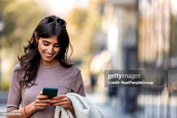 beautiful mid adult woman walking and texting message on mobile phone outside business center. - telefoon stockfoto's en -beelden